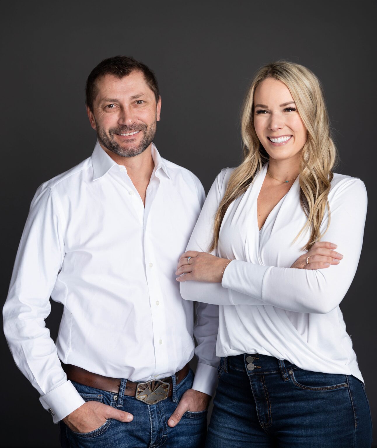 Smiling man and woman in white shirts posing against dark background.